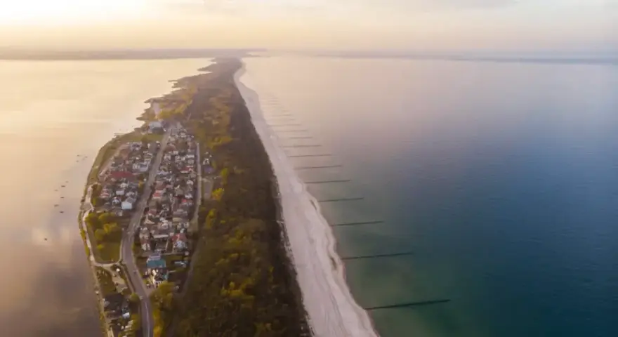 Widok z lotu ptaka na malownicze chałupy nad morzem, z piaszczystą plażą i spokojną wodą.