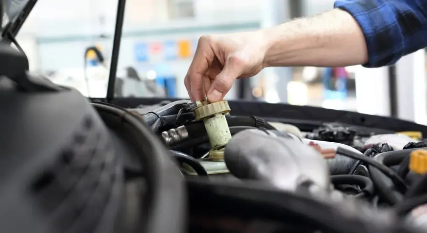Ręka mechanika dokręca korek zbiorniczka płynu hamulcowego. Czas na badanie techniczne po terminie, by uniknąć problemów.