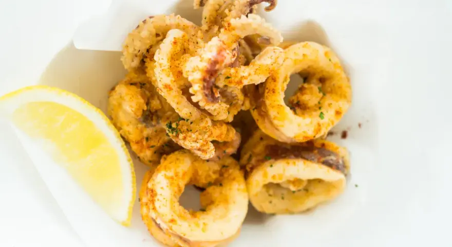 Crujientes calamares a la andaluza, dorados y sazonados, servidos con una rodaja de limón fresco.