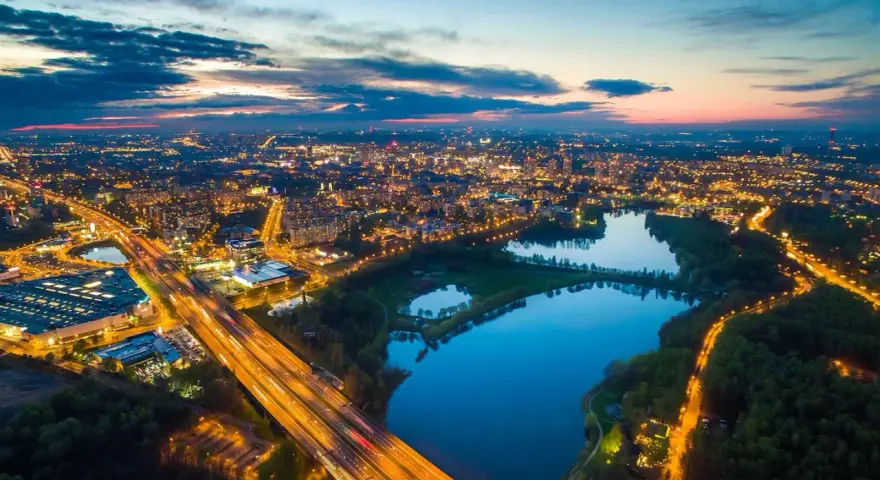 Widok z lotu ptaka na miasto nocą, z oświetloną autostradą i **trzech stawów** odbijających światła miasta.