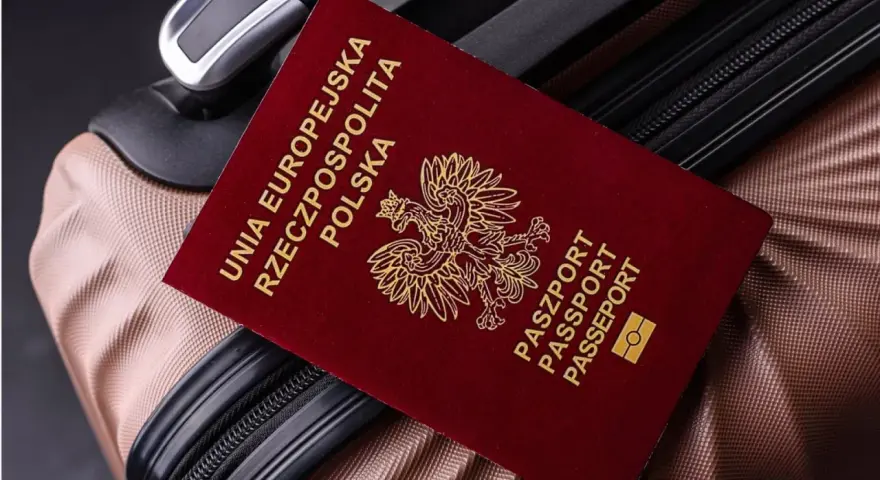 Czerwony paszport Polski z godłem orła leży na brązowej walizce.