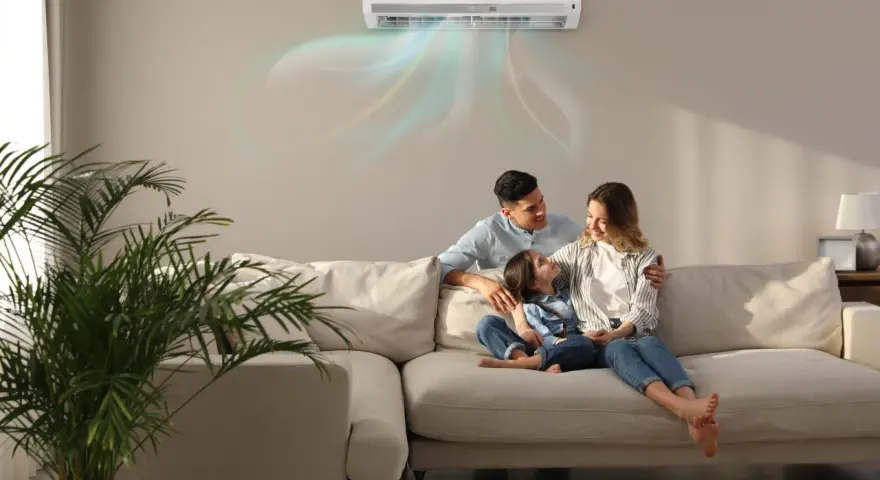 Famiglia felice sul divano, con l'aria condizionata che soffia aria fredda. Scopri come impostare condizionatore aria fredda per un comfort ottimale.