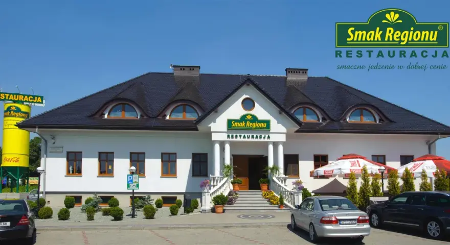 Restauracja "Smak Regionu" z białym budynkiem, schodami i samochodami na parkingu.