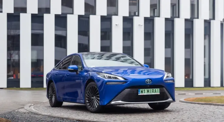 Niebieski samochód Toyota Mirai na tle nowoczesnego budynku.