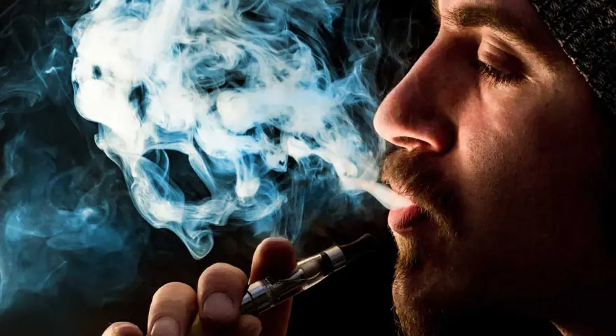 Hombre vapeando, el vaper sin nicotina es malo. El humo azul forma figuras fantasmagóricas.