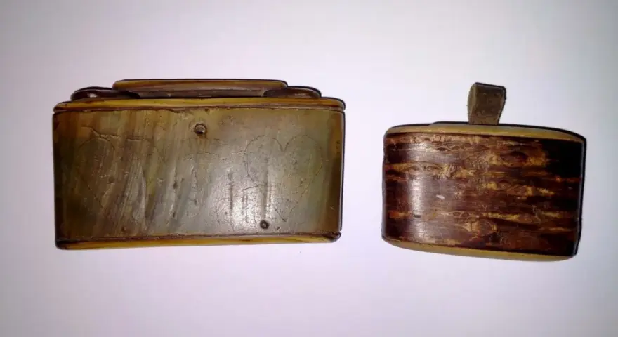 Dwie zabytkowe tabakiery z rogu, jedna z wygrawerowanymi sercami, druga z ozdobnym, drewnianym wzorem.