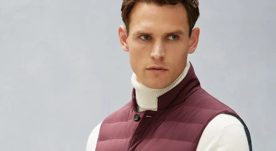 Uomo con gilet imbottito bordeaux sopra dolcevita bianco. Il gilet, un capo versatile, aggiunge stile e calore.