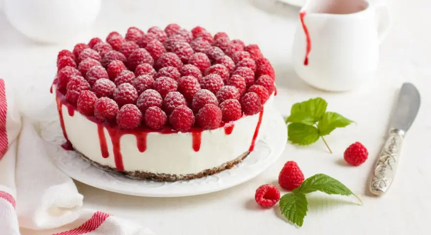 Himbeertorte mit Mascarpone, üppig belegt mit frischen Himbeeren und rotem Fruchtsirup, der über den Rand tropft.