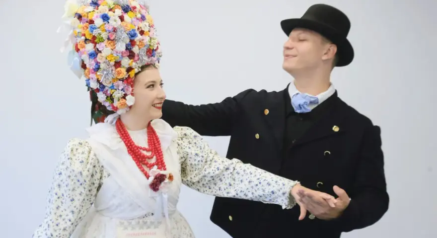 Para tańczy w strojach ludowych, co to folklor. Ona ma bogato zdobiony kwiatami wianek, on czarny kapelusz i marynarkę.