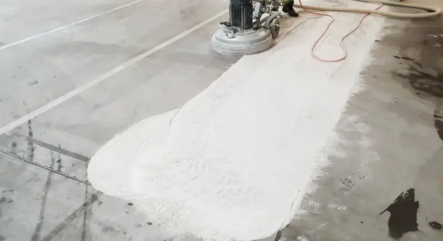 Maszyna szlifuje beton, tworząc biały pył. To etap przygotowania pod wylewkę, gdzie kluczowe są odpowiednie beton na wylewkę proporcje.