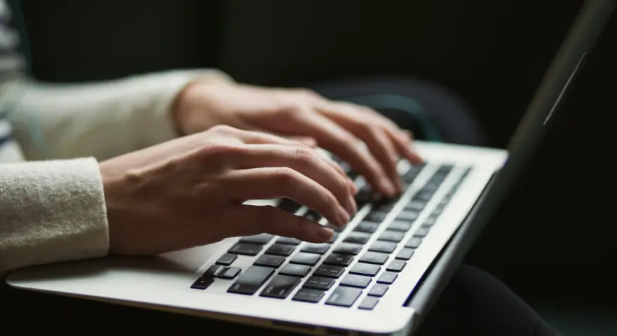 Dłonie piszą na klawiaturze laptopa, czy przed tym stawiamy przecinek? Praca zdalna w pełnym skupieniu.