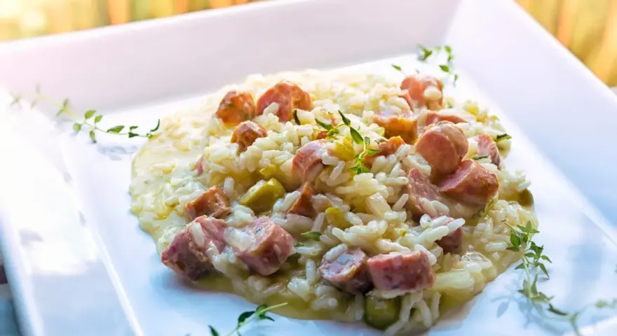 Un cremoso risotto con salsiccia, piselli e timo, servito su un piatto bianco.