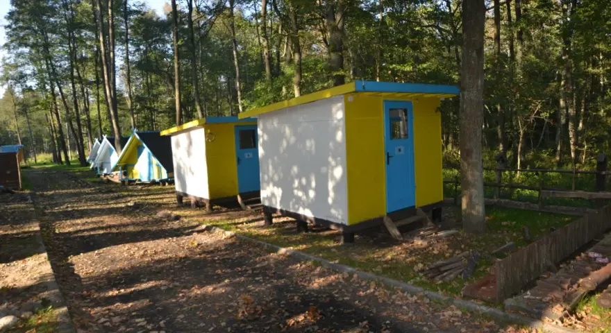 Kolorowe domki kempingowe w lesie, jak małe perły Krutyni, czekają na gości.