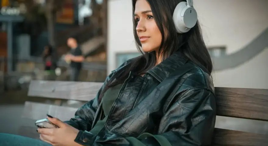 Młoda kobieta w słuchawkach, słuchająca podcastu o wymowie francuskiej, siedzi na ławce, trzymając telefon.