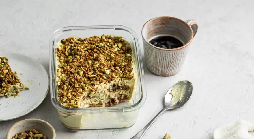Un delizioso tiramisù al pistacchio, cosparso di granella verde, pronto per essere gustato con un caffè.