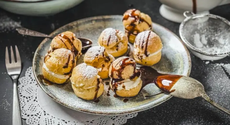 Köstliche Profiteroles, bestäubt mit Puderzucker und beträufelt mit Schokoladensauce. Ein wahrer Genuss, wie beim original profiteroles rezept.