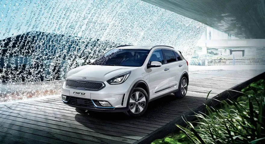 Biały Kia Niro Plug-in Hybrid na drewnianej platformie, otoczony wodnymi kaskadami i zielenią.