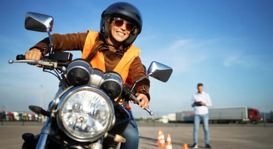Uśmiechnięta kursantka na motorze, w kasku i kamizelce, uczy się jeździć. Zastanawiasz się, ile kosztuje prawo jazdy na motor?
