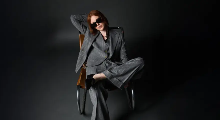 Donna con outfit giacca doppiopetto donna a righe grigie, occhiali da sole, seduta su una poltrona di pelle.