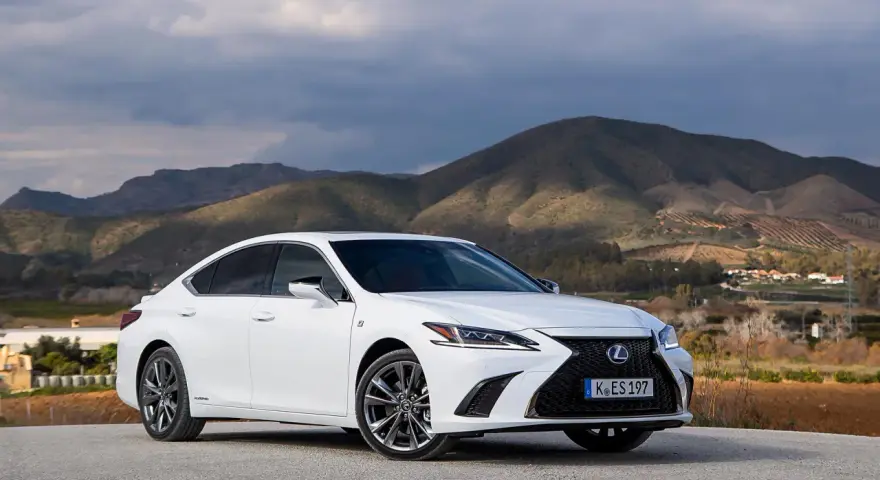 Biały Lexus ES 300h zaparkowany na tle górskiego krajobrazu. Elegancki sedan prezentuje się okazale na tle natury.