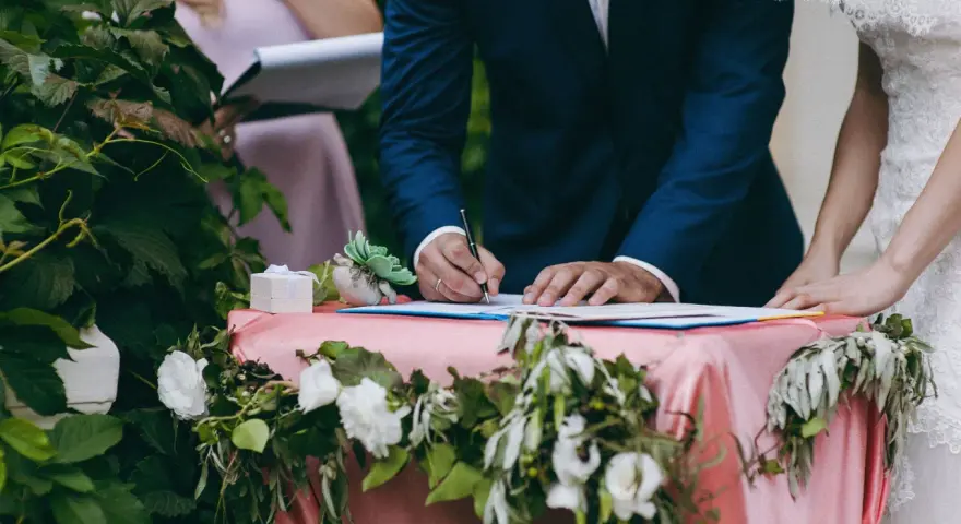 Pan młody podpisuje dokumenty, a obok stoi panna młoda. Zastanawiasz się, ile kosztuje ślub cywilny?