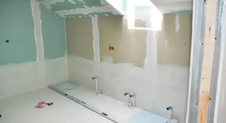 Chantier de salle de bain : murs en plaques de plâtre, tuyauterie apparente, niveau à bulle et outils au sol. Travaux d'isolation salle de bain en cours.