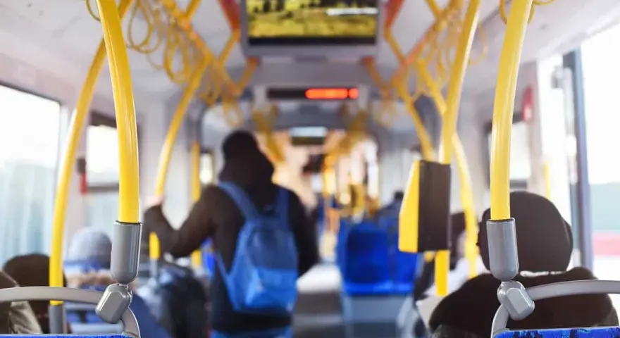 Wnętrze autobusu z żółtymi poręczami. Młody mężczyzna z niebieskim plecakiem idzie do tyłu. Uważaj, by nie dostać mandatu za brak biletu.