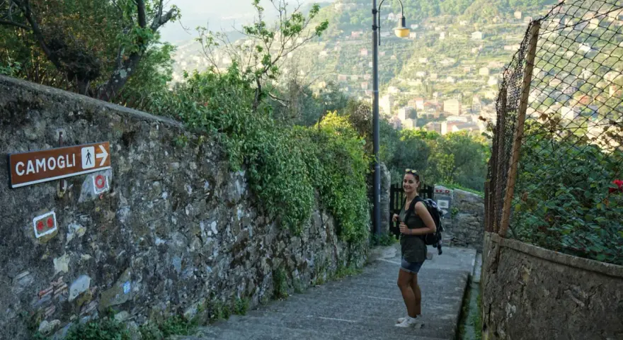 Una ragazza con zaino su un sentiero panoramico, con un cartello che indica Camogli. Perfetto per chi cerca dove dormire sul Cammino del Tigullio.