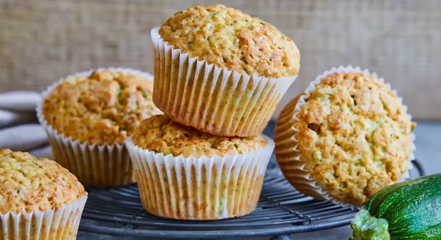 Saftige zucchini-muffins auf einem Gitter, daneben eine frische Zucchini.