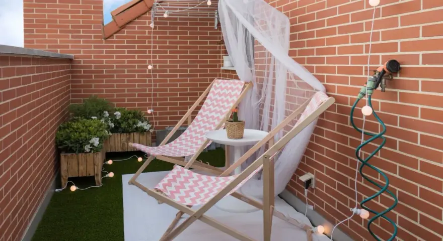 Acogedora terraza de 10 metros cuadrados con dos tumbonas, plantas y luces decorativas. Ideal para relajarse.