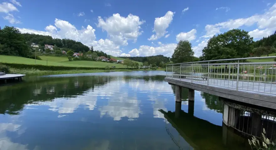 Idyllischer badesee waldhausen mit Steg und Spiegelung der Wolken im ruhigen Wasser.