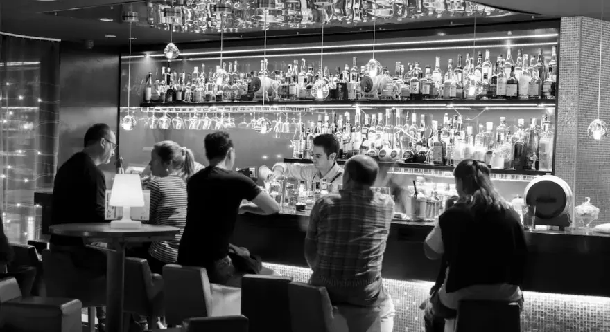 Gente en un bar cine, con un camarero sirviendo bebidas detrás de la barra llena de botellas.
