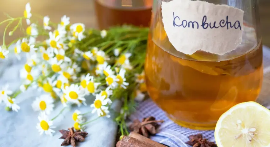 Bouteille de kombucha ambré, décorée de camomille, d'anis étoilé, de bâtons de cannelle et d'une tranche de citron.
