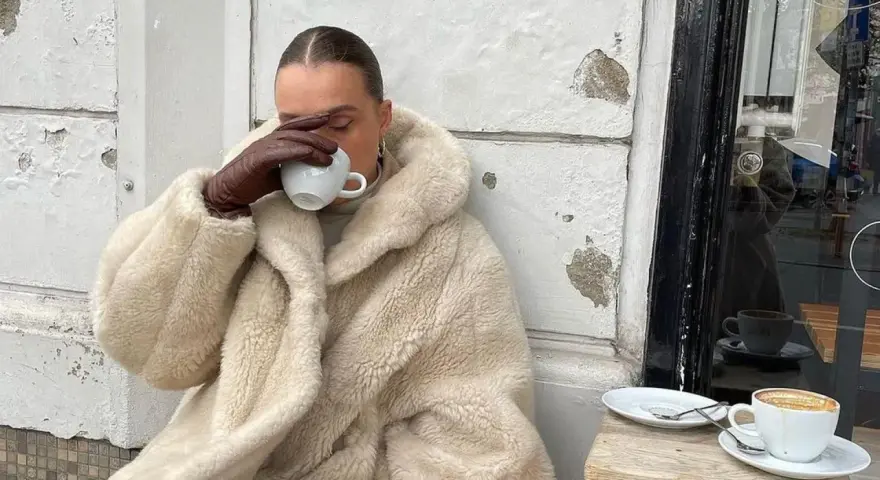 Vanilla girl w kremowym futrze pije kawę, otulona ciepłem i spokojem.