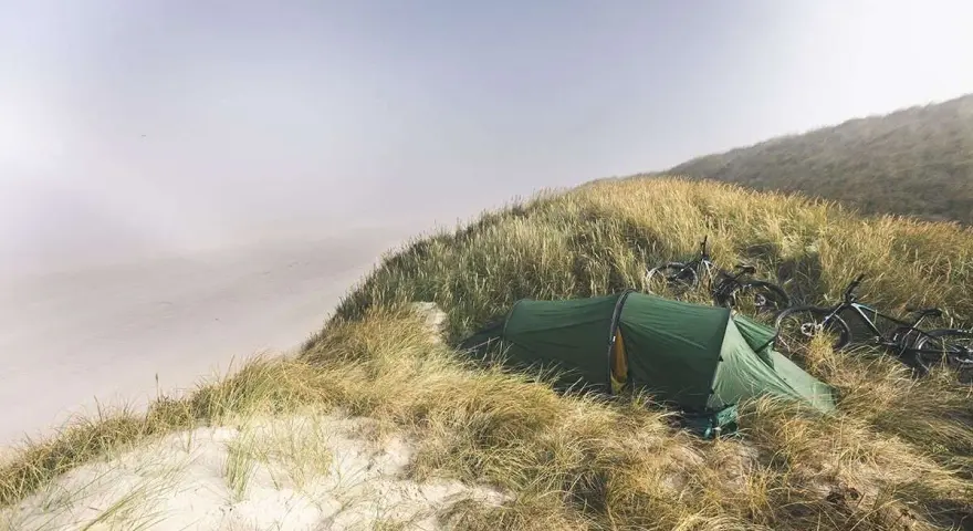 Grön tält och cyklar på en gräsbevuxen sanddyn vid havet. En idyllisk plats för äventyr i sanddynerna Danmark.