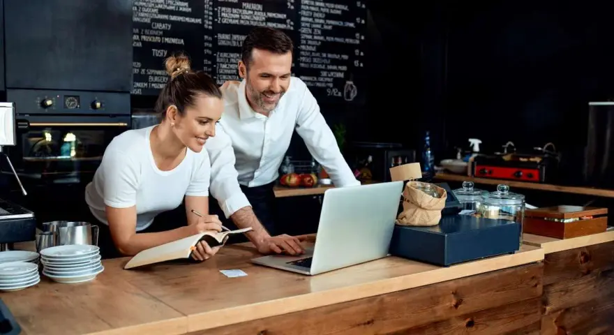 Pareja revisa menú en laptop, planificando su negocio de hostelería en España.