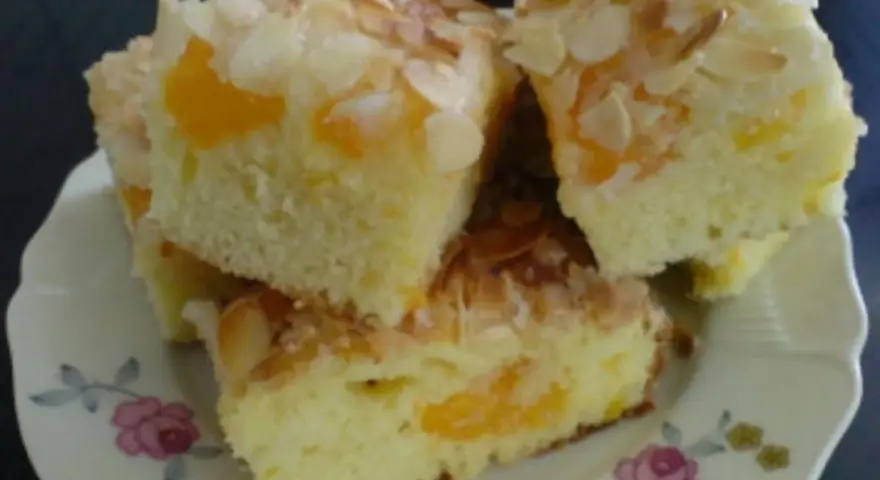 Saftiger Mandarinen Kuchen mit Mandelblättchen, auf einem Teller mit Blumenmuster.