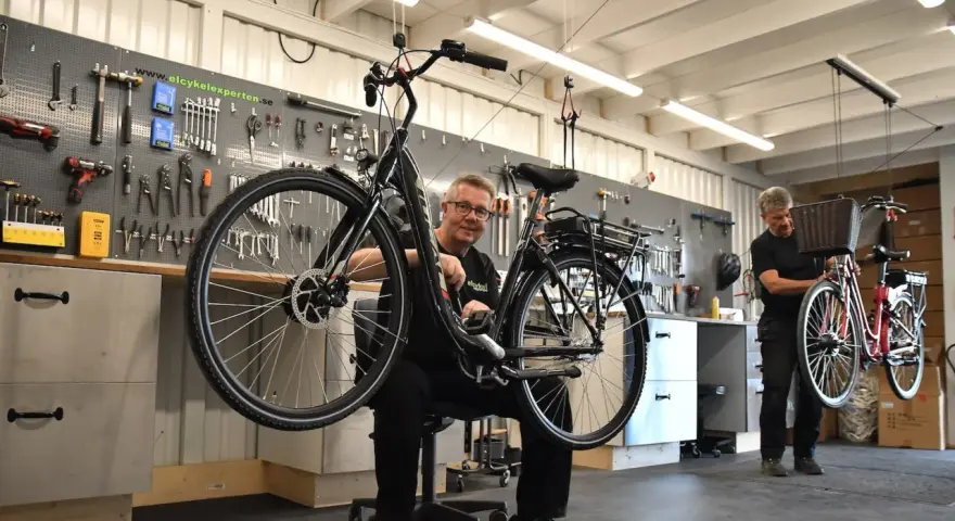 Mekaniker arbetar med en elcykel i verkstad. Verktyg på väggen visar att detta är en plats för bidrag till elcykel.