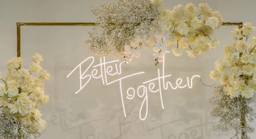 Elegancka ściana z kwiatów w kremowych odcieniach, ozdobiona neonowym napisem "Better Together".