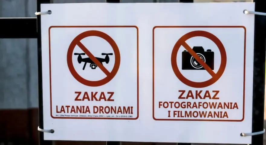 Dwa znaki na płocie: zakaz latania dronami i zakaz fotografowania i filmowania.