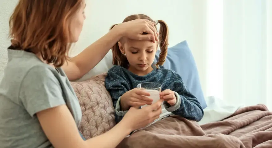 Mutter prüft Fieber bei krankem Kind im Bett. Die Krankschreibung für die Schule ist nötig, damit das Kind sich erholen kann.