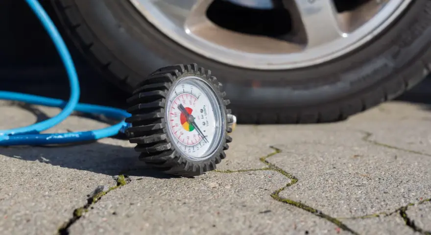 Manomètre de pression des pneus à côté d'une roue de voiture et d'un tuyau bleu.