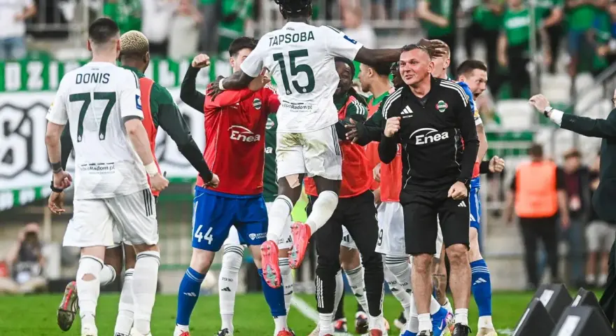 Piłkarze w białych i czerwonych strojach świętują na boisku, jeden z nich w powietrzu.