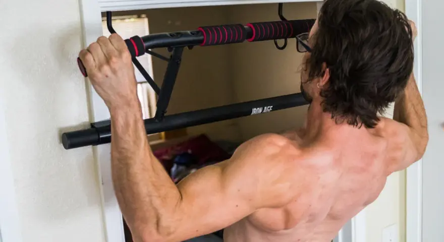 Homme musclé s'entraînant avec une barre de tirage porte d'entrée. Avis : installation facile et solide pour un entraînement efficace.
