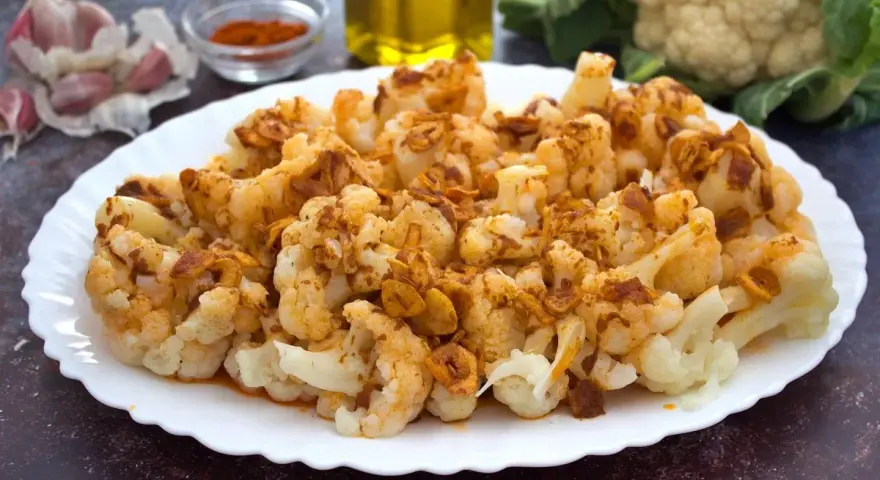 Coliflor al ajillo servida en un plato blanco, con ajo laminado y pimentón espolvoreado.