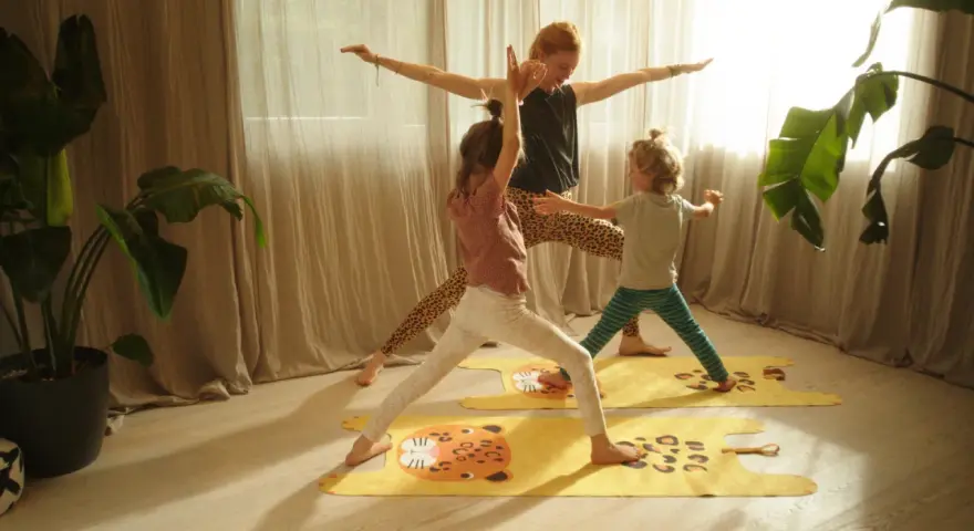 Eine Frau und zwei Kinder üben Yoga auf bunten Matten. Die Kinder haben Spaß bei den Yoga-Übungen.
