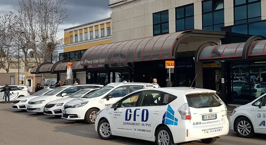 Reihe weißer Taxis vor einem Gebäude mit Taxischildern.