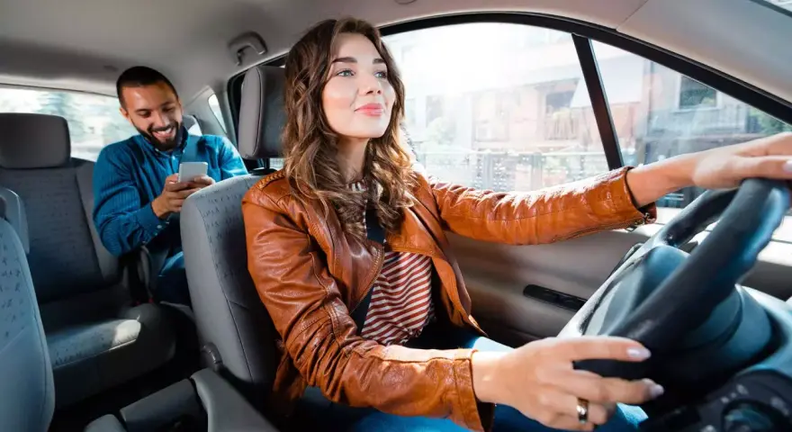 Fahrerin im Taxi, ihr Fahrgast schaut aufs Handy. Sie hat ihren Taxi Schein gut sichtbar.