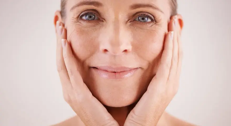 Visage d'une femme aux mains sur les joues, montrant les signes du temps et les défis des problèmes de peau et ménopause.
