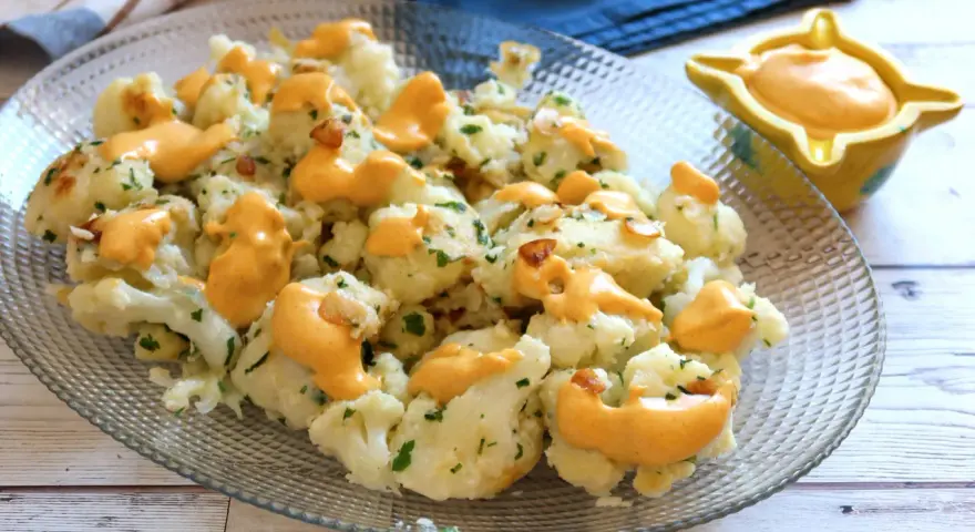 Coliflor al ajillo con salsa cremosa, adornada con perejil fresco y trocitos de ajo crujiente.